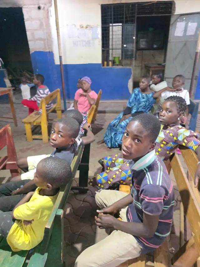 Children from New Hope sitting on wooden benches, waiting to learn